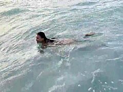 Monika Fox nada en el Océano Atlántico y posa desnuda en una playa pública con cabello largo y piercings como estrella porno milf morena.